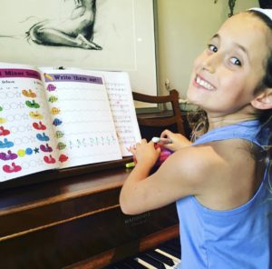 Young girl smiling at her piano theory book Cascade Method