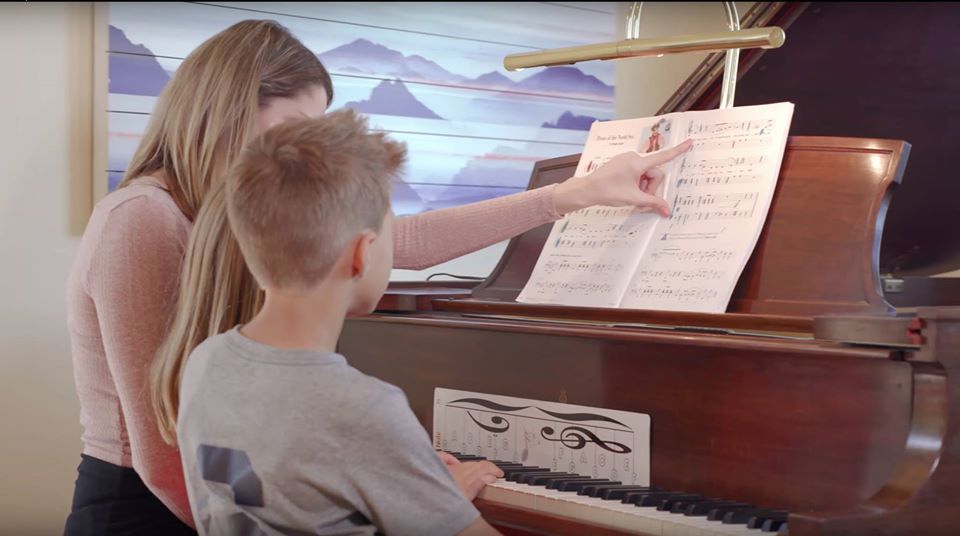 Piano teacher with two students, pointing to sheet music