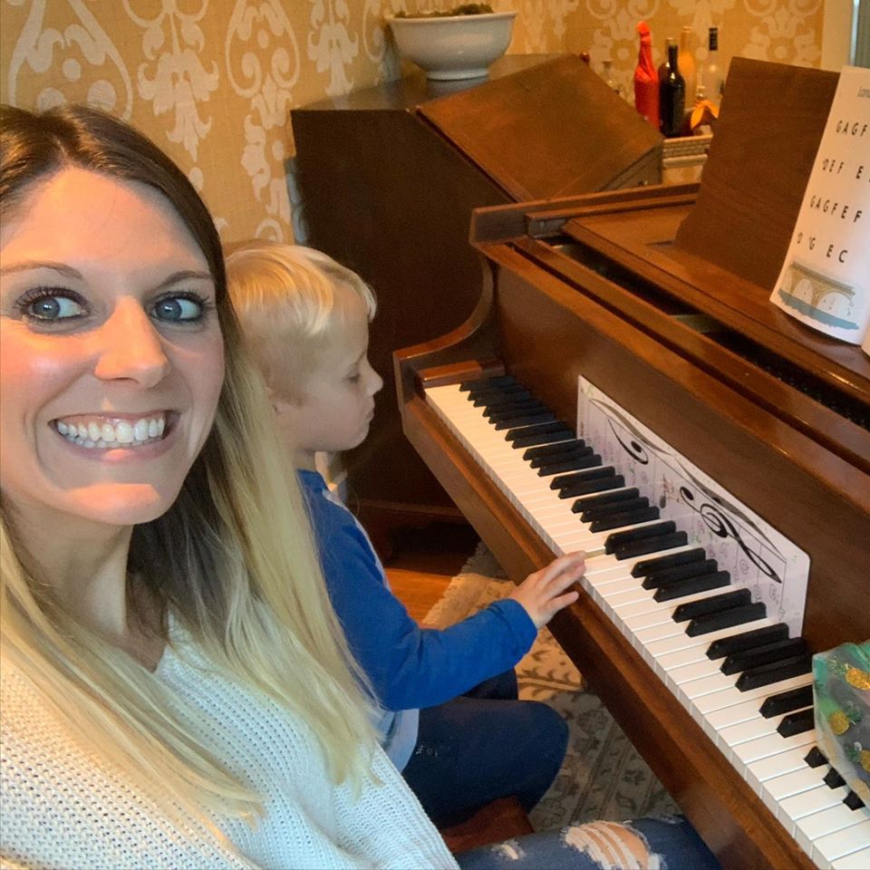 Tara smiling with her student while he plays the piano