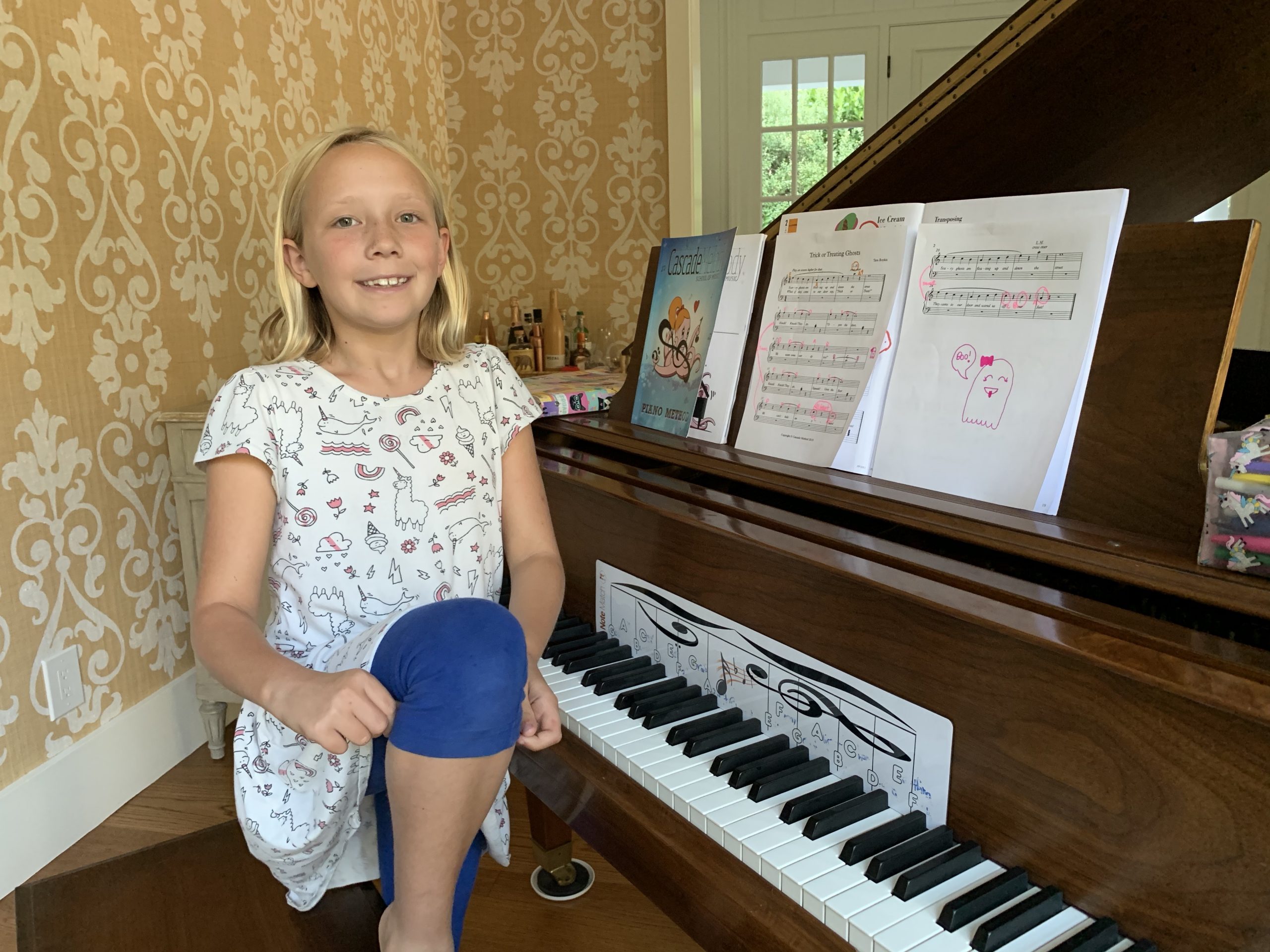 Student smiling at the piano with her cascade method theory book, notematch, and chords 1 book